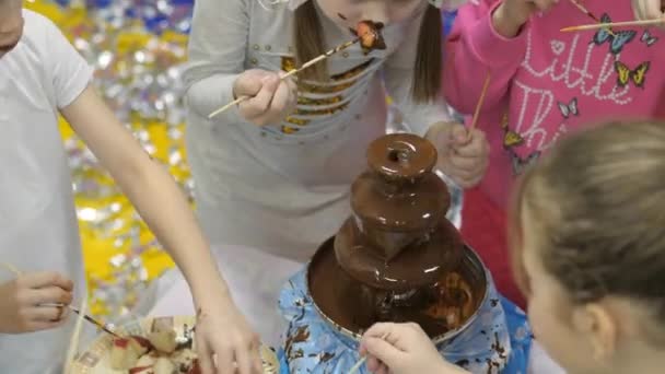 Sala de juegos para niños. Los niños comen chocolate de una fuente de chocolate . — Vídeos de Stock