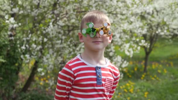 メガネのスピナーが回転しています 通りで楽しい おかしな顔に回転するおもちゃ 桜の花を咲かせる背景の子供 — ストック動画