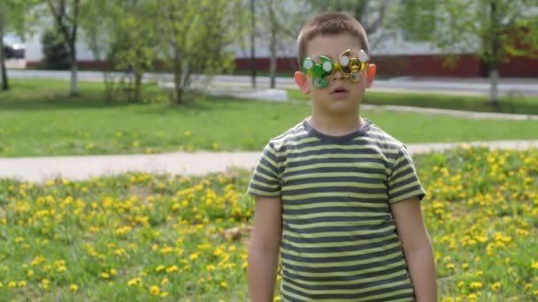 Spinner on the glasses is spinning. Fun on the street. Boy on a background of yellow flowers, dandelions. — Stock Video