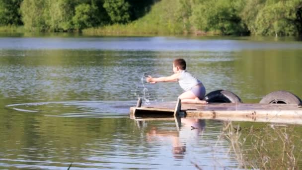 Molo nad rzeką. Dzieci rozpryskiwania wody na molo. — Wideo stockowe