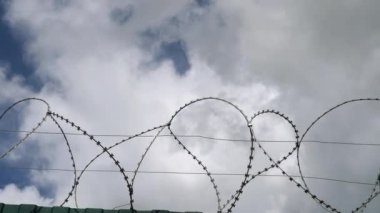 Beyaz bulutlar ile mavi gökyüzüne karşı dikenli tel.