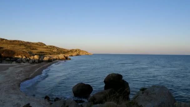 Le onde del mare lavano la spiaggia di sabbia. Una scogliera rocciosa sporge in mare. Il cielo cambia colore . — Video Stock