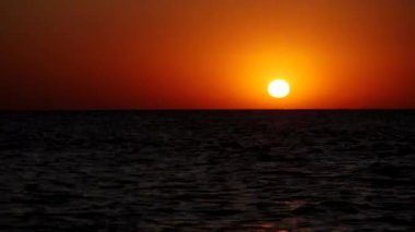 Kırmızı güneş ufukta okyanusa doğru batıyor. Bir gök cismi denize batar..