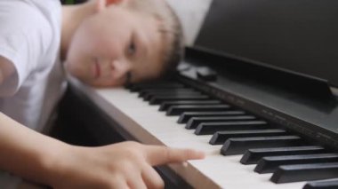 Elektronik piyano. Parmaklar piyano tuşlarına bassın. Müzik dersi. Çocuk derste yorgundu ve enstrümanın tuşlarına uzandı. Çocuk tembelce müzikle meşgul..