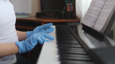 Elektronik piyano. Parmaklar piyano tuşlarına bassın. Eldivenli eller. 2020 salgını, kendini izole etme. Çocuk elleri piyano klavyesinde. Yan görünüm.