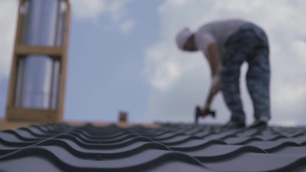 屋顶工程 装配工把金属砖钉在房顶的板条箱上 屋顶建设 私人住宅的屋顶有一半被金属覆盖着 模糊中的那个人 在乌云密布的蓝天下 一个模糊的人影 — 图库视频影像