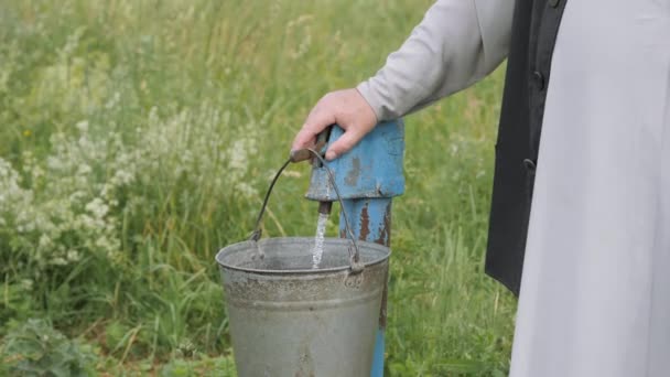 긴 셔츠 를 입은 사람 이 펌프에서 물을 금속 바케 츠 에 붓는다. — 비디오
