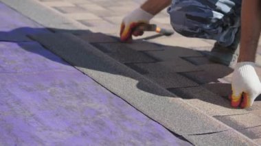 Çatı işi. Özel bir evin çatısına yumuşak bir çatı sermek. Esnek çatı malzemeleriyle çalışıyor. Çatıyı çivi ve çekiçle tamir etmek. Yumuşak döşeme tablosunun hizalanması.