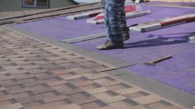 Çatı işi. Özel bir evin çatısına yumuşak bir çatı sermek. Esnek çatı malzemeleriyle çalışıyor. Çatıyı çivi ve çekiçle tamir etmek. Yumuşak döşeme tablosunun hizalanması.