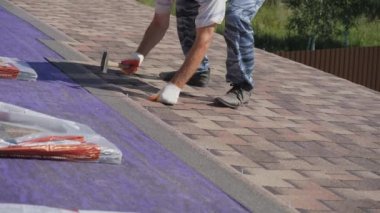 Çatı işi. Özel bir evin çatısına yumuşak bir çatı sermek. Esnek çatı malzemeleriyle çalışıyor. Çatıyı çivi ve çekiçle tamir etmek. Yumuşak döşeme tablosunun hizalanması.