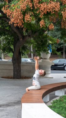 Oğlan iki elini ağacın dallarına doğru çeker. Şehir ortamında sabun ağacı. Orijinal üç lob şeklindeki meyveler kırmızımsı-kahverengidir. Çocuk bankta oturuyor..