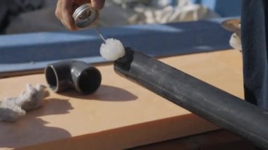 Plastik bir borunun ucuna yapıştırıcı sürüyorum. Soda arasında su boruları bağlanıyor. Boru kıvrımının kurulumu. Özel havuz suyu tedarik sistemi kurulmadan önce hazırlayıcı bir iş. Su için bir PVC plastik boru bölümü kurulumu.