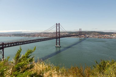 25 Nisan 'da Lizbon' daki köprüde Tejo nehri üzerinde hareket eden arabalarla. Güneşli bir gün ve modern bir bina manzarası..