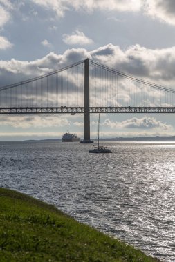 25 Nisan 'da Lizbon' daki köprüde Tejo nehri üzerinde hareket eden arabalarla. Güneşli bir gün ve modern bir bina manzarası..
