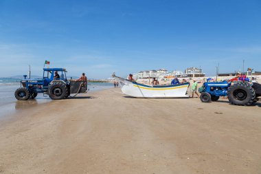 Costa da Caparica, Portekiz - 10 Eylül 2020: Bir grup balıkçı traktör kullanarak turist plajından balık avlıyor. Tatilciler izler ve yardım eder..