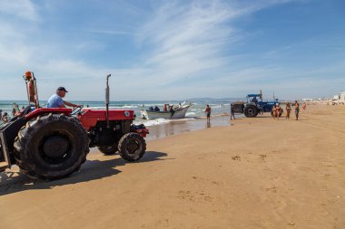 Costa da Caparica, Portekiz - 10 Eylül 2020: Bir grup balıkçı traktör kullanarak turist plajından balık avlıyor. Tatilciler izler ve yardım eder..