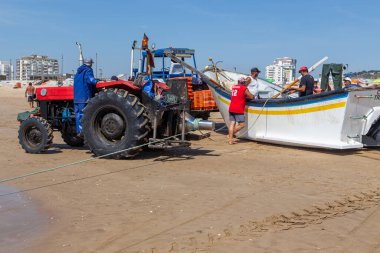 Costa da Caparica, Portekiz - 10 Eylül 2020: Bir grup balıkçı traktör kullanarak turist plajından balık avlıyor. Tatilciler izler ve yardım eder..