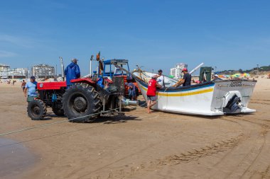 Costa da Caparica, Portekiz - 10 Eylül 2020: Bir grup balıkçı traktör kullanarak turist plajından balık avlıyor. Tatilciler izler ve yardım eder..
