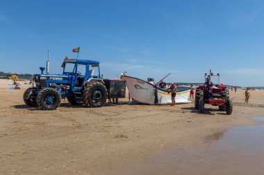 Costa da Caparica, Portekiz - 10 Eylül 2020: Bir grup balıkçı traktör kullanarak turist plajından balık avlıyor. Tatilciler izler ve yardım eder..