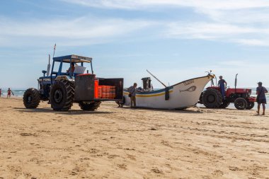 Costa da Caparica, Portekiz - 10 Eylül 2020: Bir grup balıkçı traktör kullanarak turist plajından balık avlıyor. Tatilciler izler ve yardım eder..
