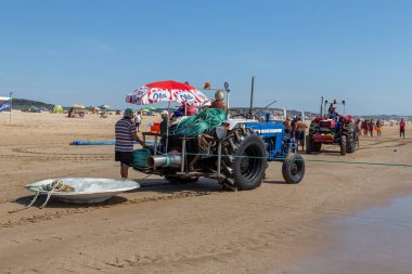 Costa da Caparica, Portekiz - 10 Eylül 2020: Bir grup balıkçı traktör kullanarak turist plajından balık avlıyor. Tatilciler izler ve yardım eder..