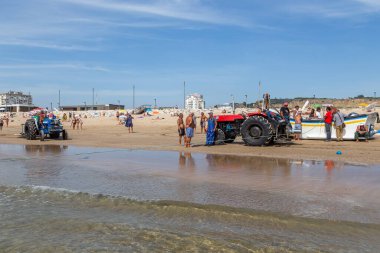 Costa da Caparica, Portekiz - 10 Eylül 2020: Bir grup balıkçı traktör kullanarak turist plajından balık avlıyor. Tatilciler izler ve yardım eder..