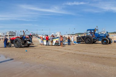 Costa da Caparica, Portekiz - 10 Eylül 2020: Bir grup balıkçı traktör kullanarak turist plajından balık avlıyor. Tatilciler izler ve yardım eder..