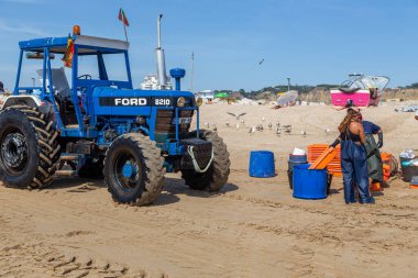 Costa da Caparica, Portekiz - 10 Eylül 2020: Bir grup balıkçı traktör kullanarak turist plajından balık avlıyor. Tatilciler izler ve yardım eder..