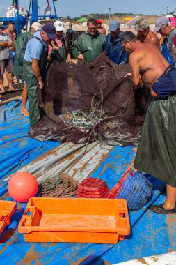 Costa da Caparica, Portekiz - 10 Eylül 2020: Bir grup balıkçı traktör kullanarak turist plajından balık avlıyor. Tatilciler izler ve yardım eder..