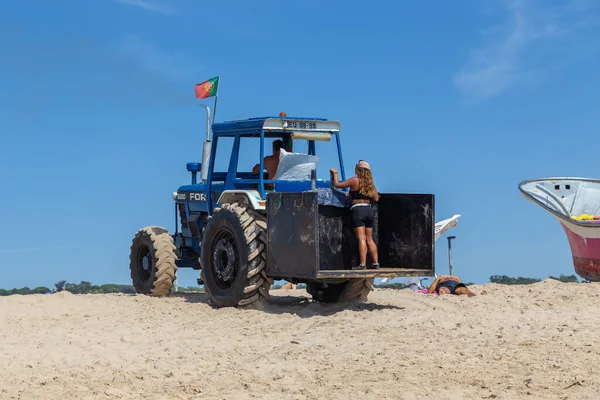 Costa da Caparica, Portekiz - 10 Eylül 2020: Bir grup balıkçı traktör kullanarak turist plajından balık avlıyor. Tatilciler izler ve yardım eder..