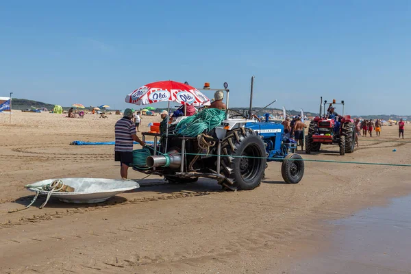 Costa da Caparica, Portekiz - 10 Eylül 2020: Bir grup balıkçı traktör kullanarak turist plajından balık avlıyor. Tatilciler izler ve yardım eder..
