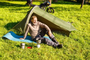 Yaşlı turistik bir çay yakınındaki ormanda çadırını üzerinde güneşli yaz günü soba bir Portable kaynar