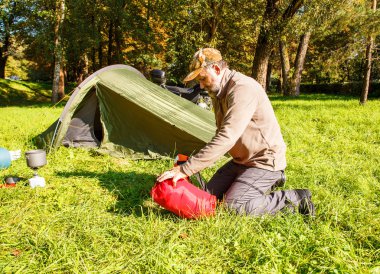 Yaşlı turist foldjng güneşli yaz gününde ormandaki bir çadır