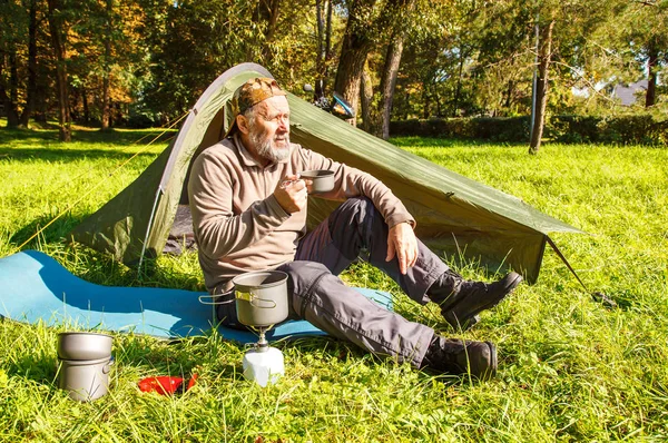 Yaşlı Turizm güneşli yaz gününde orman çadırında yakınındaki metal bir kupa çay içme