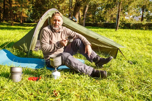 Yaşlı Turizm güneşli yaz gününde orman çadırında yakınındaki metal bir kupa çay içme