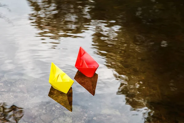 two multicolored paper boats floating on a stream outdoor on autumn day closeup