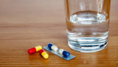 tıbbi kapsüller ve masada bir bardak su