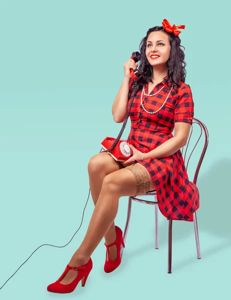 Sorrindo jovem pinup mulher sentada em uma cadeira e falando no phon — Fotografia de Stock