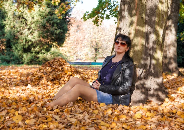 Sonbaharda parkta çimüzerinde oturan genç kadın — Stok fotoğraf