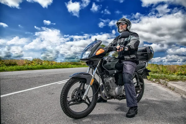açık yolda motosikletinin üzerinde oturan yaşlı motosikletçi