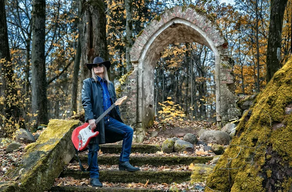 Oudere langharige man met gitaar in een donker bos — Stockfoto