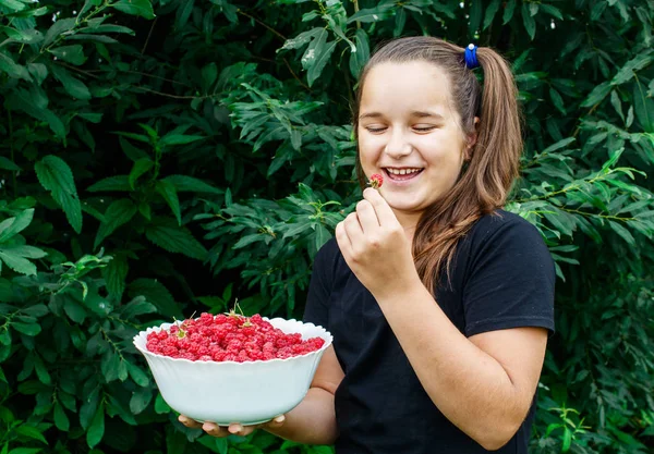 Adolescente chica sosteniendo un tazón de frambuesas en el jardín — Foto de Stock