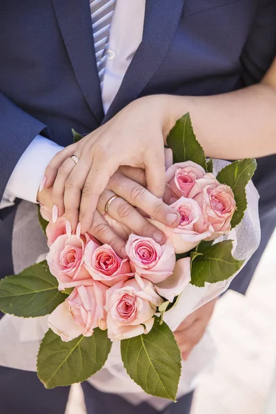 Mani degli sposi con anelli e un mazzo di rose — Foto Stock