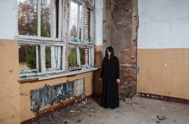 Siyah elbiseli genç, güzel gotik kadın terk edilmiş bir evin kırık penceresinin yanında duruyor.