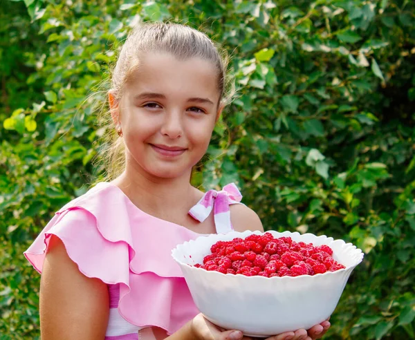 ピンクのドレスを着た美しい笑顔の十代の女の子晴れた夏の日に庭で熟したラズベリーの皿を保持 — ストック写真