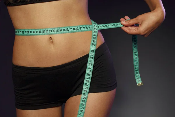 Спортивна струнка жінка вимірює талію за мірною стрічкою після дієти на темно-сірому фоні — стокове фото