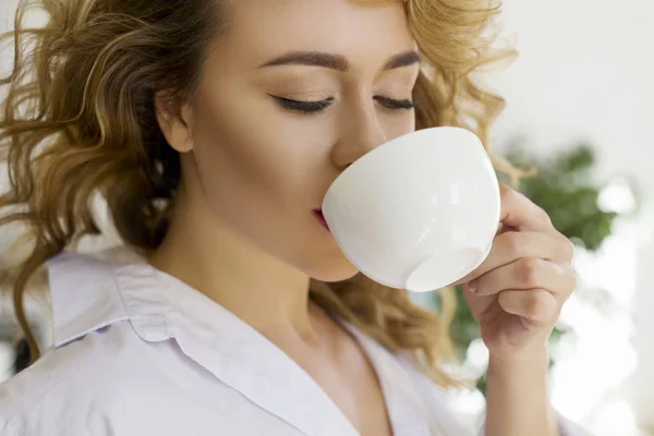 Portret młodej blondynki w jasnej kuchni pijącej herbatę lub kawę — Zdjęcie stockowe