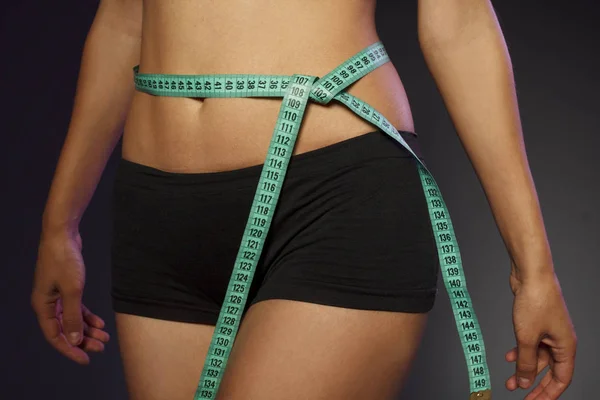 Спортивна струнка жінка вимірює талію за мірною стрічкою після дієти на темно-сірому фоні — стокове фото