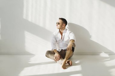 Yakışıklı esmer adam, gün ışığında stüdyoda poz veriyor.