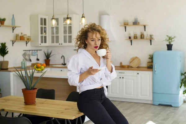 Portret van jonge blonde vrouw in lichte keuken drinken van thee of koffie — Stockfoto